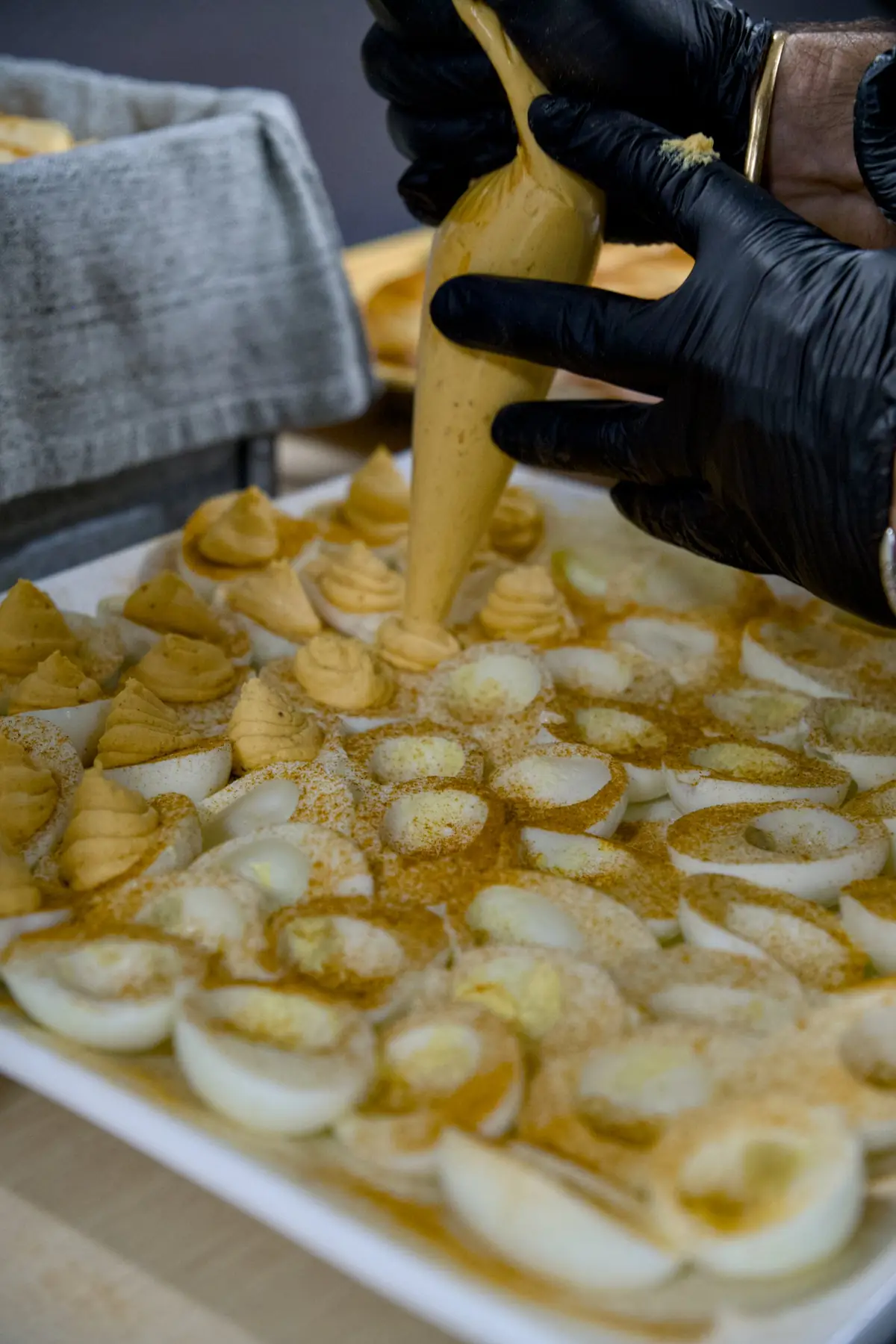 Gloved hands piping filling into a platter of spice-dusted deviled eggs