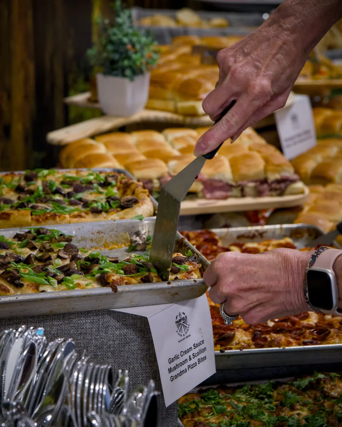 A guest lifting a square of garlic cream sauce mushroom and scallion grandma pizza from a tray labelled with a Pairfield Pizza & Pints place card