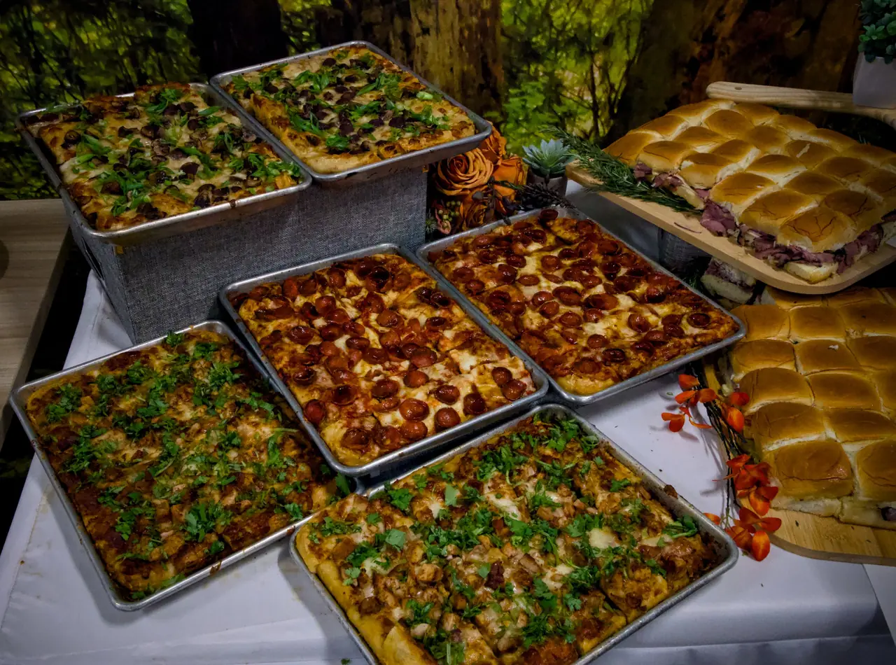 Trays of mushroom, pepperoni and butter chicken grandma pizza beside roast beef sliders at a catered buffet