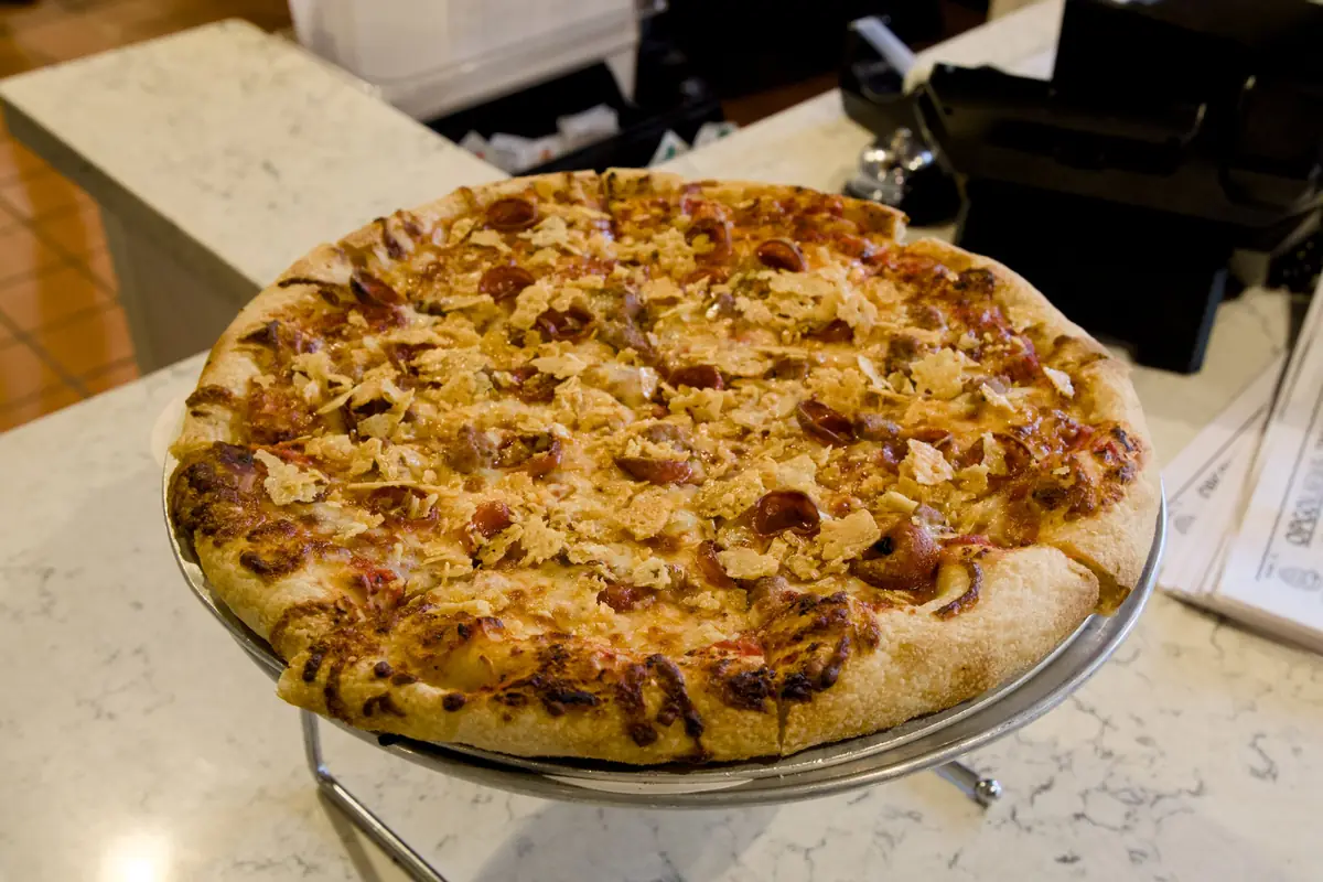 A pepperoni and sausage pizza topped with crispy cheese on a serving stand at Pairfield Pizza & Pints