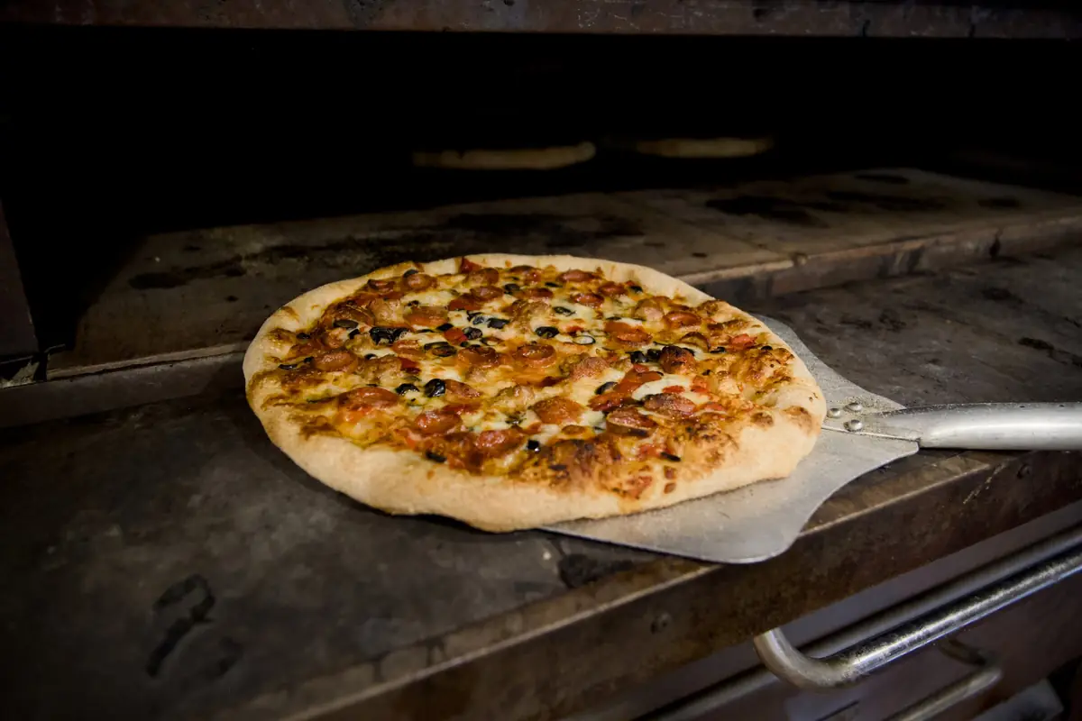 A pizza with pepperoni, sausage, black olives and red peppers on a peel at the mouth of the oven at Pairfield Pizza & Pints